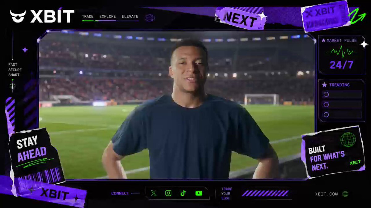 The image shows a man standing in front of a soccer stadium, smiling at the camera while wearing a blue shirt. The background features a soccer field with players visible in the distance. The image also includes text that reads "XBIT", which is likely related to the content displayed on the screen or the post itself.