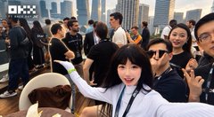 A young woman with dark bangs smiles and gives two thumbs up to the camera at an outdoor event, with a crowd of people behind her and the logo 'OLX' visible in the top left corner.
