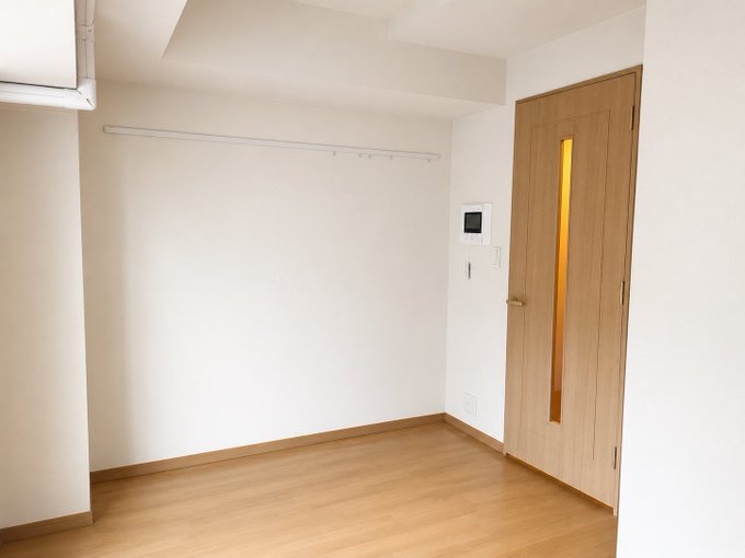 An empty, freshly vacated room with light wood flooring, white walls, a wall-mounted air conditioner, and a wooden door with a narrow vertical window—fittingly capturing the moment after moving out of a long-time Nihonbashi apartment, right before a dispute with the management company over unfair charges.