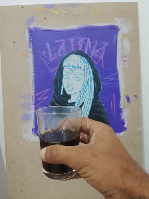 Hand holding a glass of dark liquid in front of a purple-painted artwork depicting a hooded figure with the text "HI NAT" visible in pink.