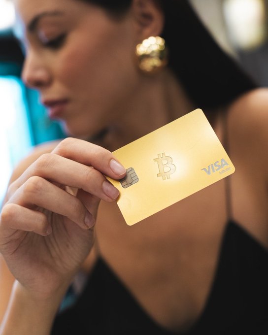 A stylized image of a woman in profile wearing gold earrings, holding a gold Visa credit card prominently featuring the Bitcoin logo and a chip.
