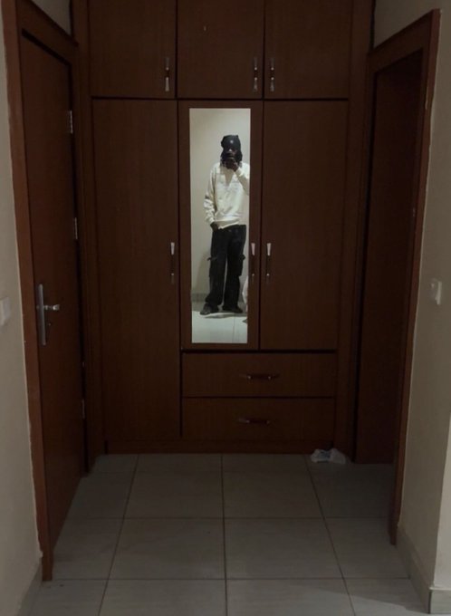 A young person stands in front of a mirror built into a dark wooden wardrobe, holding a camera to take a selfie in a dimly lit hallway. The post celebrates the 19-year-old's birthday with pride, and the image appears to be their birthday post showcasing their age milestone.