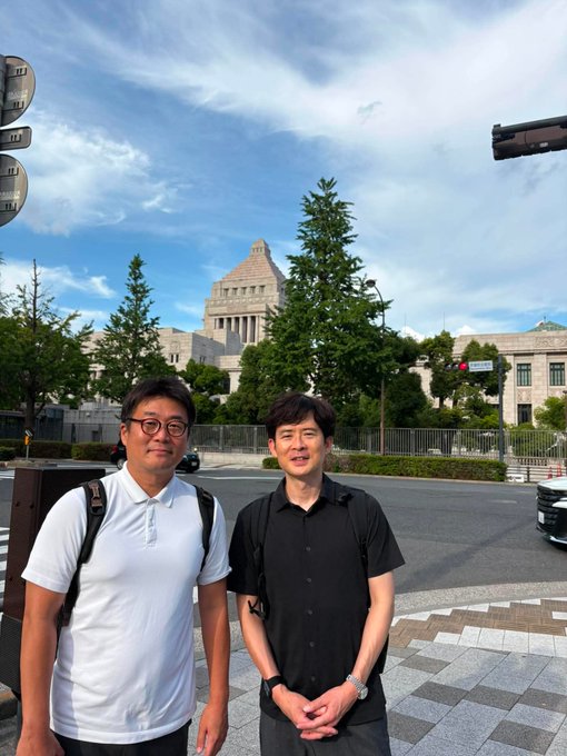 Two men pose for a photo in front of the National Diet Building in Tokyo, with the post highlighting their discussion about the future of using stablecoins to pay taxes in Japan.