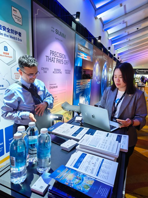 Two professionals staff a Summit 'Precision That Pays Off' booth offering Crypto Tax, Business Accounting, and Portfolio Tracking services, surrounded by marketing materials and water bottles at a convention.