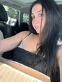 A selfie of a woman with long dark hair wearing a black tank top, seated inside a car.