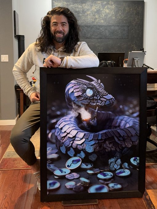 A man poses with a framed artwork of a snake coiled among coins wearing what appears to be an Iron Man-style helmet, the prized piece he plans to hang once his SNEk cryptocurrency reaches a $1B valuation.