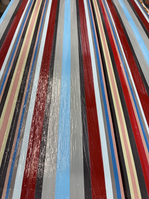 A close-up photograph of a glossy surface featuring vertical stripes in various colors including red, blue, black, gray, white, and tan.