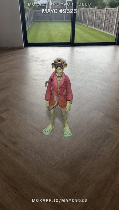 A toy figure of a green-skinned character in a red jacket and pilot goggles stands on a wooden floor, with text reading 'MUTANT APE YACHT CLUB', 'MAYC #9523', and 'MOXAPP.IO/MAYC9523'.