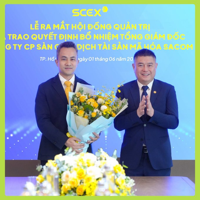 Two men in suits pose at an SCEX event in Ho Chi Minh City on June 1st, with one holding a bouquet of flowers against a backdrop announcing the launch of the Board of Directors and the appointment of the General Director of SCEX (Sacom Cryptocurrency Asset Exchange JSC), coinciding with the company's major capital increase to 5,000 billion VND.