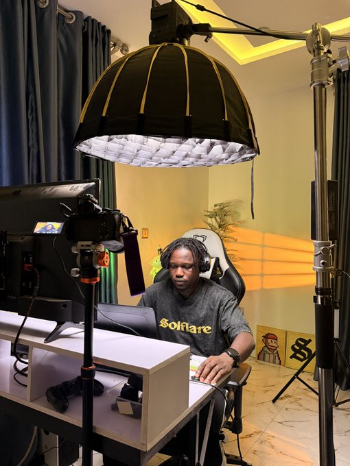 A man wearing a 'Solflare' t-shirt and headphones sitting in a streaming chair under a large softbox light setup in a home studio.