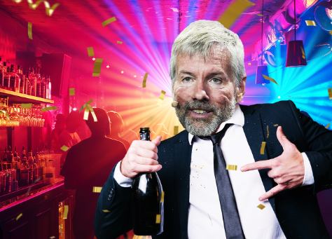 A gray-bearded man in a black suit celebrates with a bottle at a bar with colorful lighting and confetti.