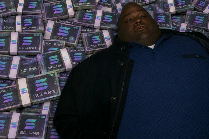 A man lies among stacks of Solana (SOL) branded boxes on a black background, in a parody-style image reminiscent of wealth flexing memes.