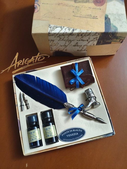 An 'Arigato' gift set containing a blue quill pen, ink bottles labeled 'Fonte di Rialto Venezia', and a small gift box with a blue ribbon.