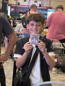 A young boy smiles excitedly at the NSCC (National Sports Collectors Convention) show, proudly holding up a Veefriends Farm Fights Shrewd Sheep trading card, presumably the 1/1 auto pulled by AlDadsnet as mentioned in the post.