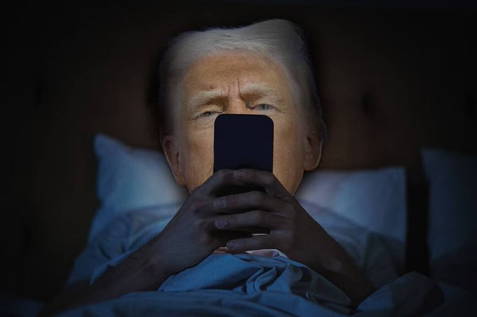 An older man with white hair lies in bed in a dark room, holding a phone in front of his face illuminated by the screen's blue glow.