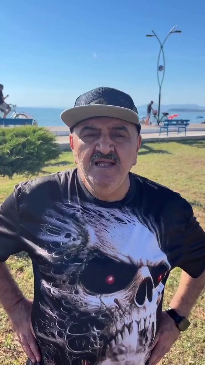 The image features a man wearing a skull t-shirt, standing outdoors with his hands on his hips. The photo has been captioned "Evet. Ethereum 881 beklentime doğru adim yol aliyor:". This suggests that the man is posing for a picture in front of a beach or ocean view, possibly at sunset.