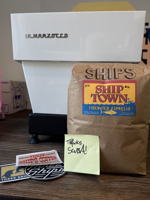 A bag of "SHIPS SHIP TOWN" Tidewater Espresso coffee next to a white La Marzocco espresso machine, with a yellow sticky note reading "Thanks Scout!!" and a "Three Ships Coffee" sticker.