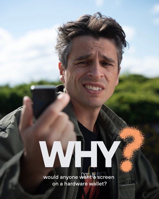 A man with messy brown hair holding up a phone with a confused expression, with text overlay reading "WHY? would anyone want a screen on a hardware wallet?"