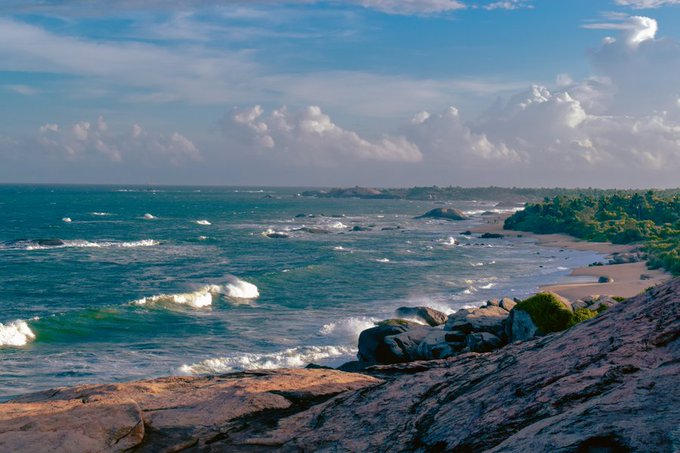 A scenic photograph captures a coastal landscape with waves crashing against rocky shores under a partly cloudy sky.