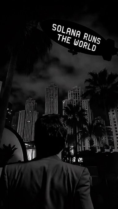 A black and white image of a man viewed from behind, looking at a city skyline with an illuminated blimp overhead reading 'SOLANA RUNS THE WORLD'.