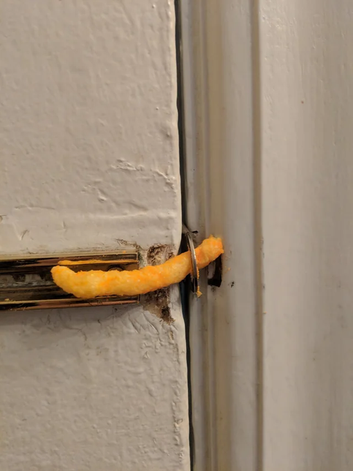 A close-up of a window latch where a piece of a cheese puff snack is wedged into the mechanism.