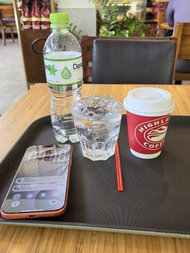 Photo of a cafe table tray containing a Dasani water bottle, a glass of ice water, a Highline Coffee cup, and a smartphone.