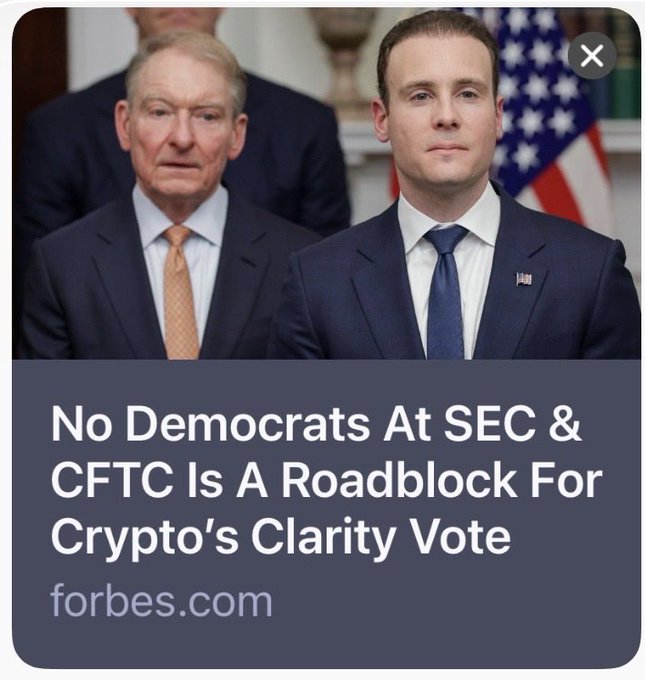 A graphic from a Forbes article titled "No Democrats At SEC & CFTC Is A Roadblock For Crypto's Clarity Vote," showing two men in suits standing in front of an American flag. The image relates to the post's discussion of how vacancies and the lack of Democratic Commissioners at the SEC and CFTC are creating obstacles for passing the crypto Clarity Act in the House.
