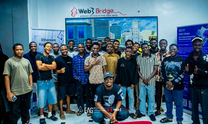 A large group of young developers poses together at the EAG Global Buildathon Nigeria event, with the "Web3Bridge" and "Africa's Access to the New Web" banner displayed prominently behind them alongside signage for "HSK Chain DeSola Financial Infrastructure," celebrating local Web3 builders developing on HSK Chain.