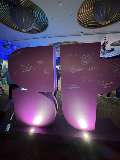 A pink illuminated display shaped like the number '57' is covered in handwritten signatures and messages, including 'KRIS', 'PITHLOS', 'FASHION AUDIT GROUP', 'Trait Hotel SOSCICNA', and 'SYP SUPERFAN BLACK'.
