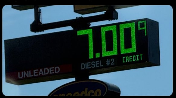 A digital gas station sign displays "7.009" in bright green LED numbers above labels for "UNLEADED," "DIESEL #2," and "CREDIT," with a Speedco logo visible below.

The image relates to the post by contrasting the rising fuel prices—nearly $7 per gallon—with Bitcoin, implying that as inflation erodes traditional currency's purchasing power, Bitcoin serves as a hedge against diminishing value.