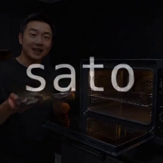 The image shows a man standing next to an open black oven, holding two plates of food inside the oven. The oven has the word "sato" written on its door, which suggests that the man might be preparing or cooking pizza using the oven.