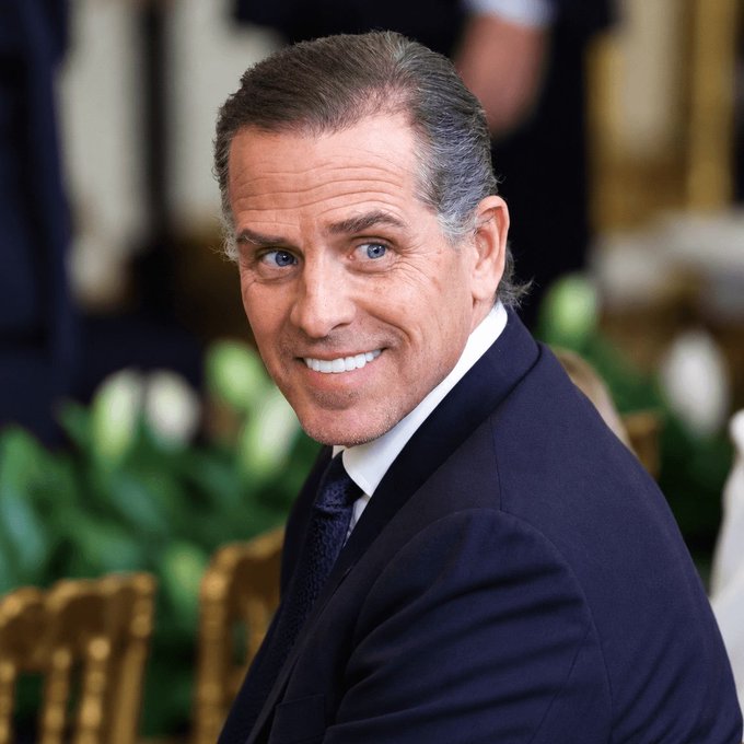 A portrait of a smiling man with graying hair wearing a dark suit and tie, photographed in an ornate setting.
