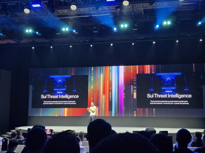 A presenter on stage at a tech conference introduces 'Sui Threat Intelligence' by Mandiant (Google Cloud), shown on large screens behind them.