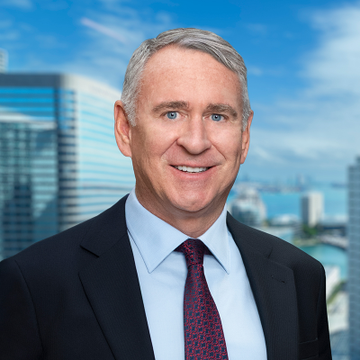 A professionally dressed man with gray hair, wearing a dark suit and a maroon tie, smiles confidently in front of a backdrop of a modern city skyline featuring glass skyscrapers and a waterfront. The polished, corporate headshot style reinforces the post's message about savvy traders executing a rapid 100% gain in just three weeks while others were left with losses.