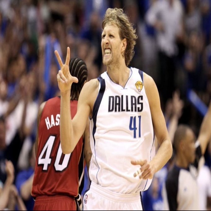 A Dallas Mavericks player wearing jersey #41 holds up three fingers in celebration, while a Miami Heat player wearing #40 (Haslem) stands in the background during an NBA game.