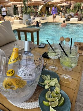 A bottle of Casa Del Mare vodka and Schweppes ginger ale sit alongside limes and cocktail glasses beside a resort pool, illustrating the post's message of cashing in market profits to enjoy a relaxing weekend escape.