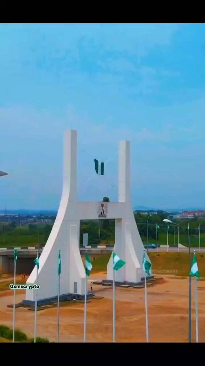 The image features a large white monument with green flags at its top, set against a backdrop of trees and an overcast sky, suggesting an outdoor event or gathering. There are multiple poles near the monument holding up the flags, which add to the festive atmosphere. The main message of the photo is likely related to the upcoming Solana Summit in Nigeria, as indicated by the caption at the bottom providing information about how custom animation was used for this image.