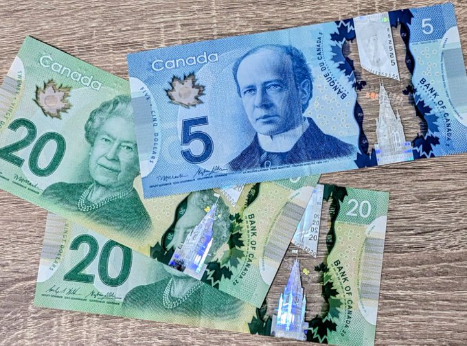 Several Canadian polymer banknotes, including $5 and $20 bills featuring King Charles III and Queen Elizabeth II, scattered on a wooden surface.