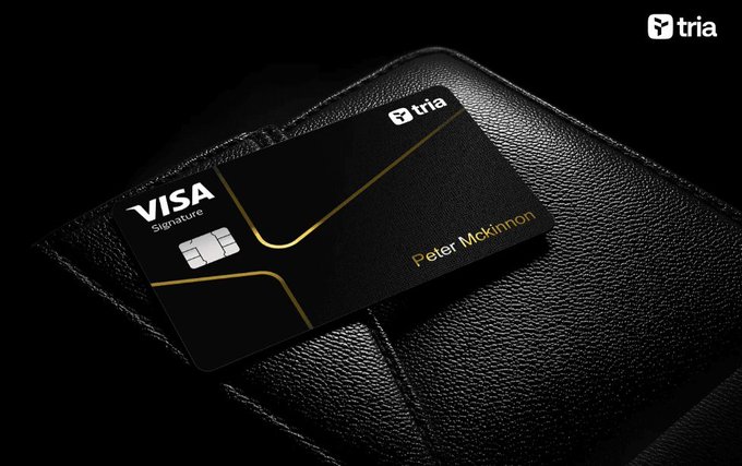 The image features a black wallet with a Visa credit card sitting on top of it, placed against a dark background. The wallet has a gold stripe running down its center, adding an elegant touch to its design. The credit card itself is black with a gold stripe running along the edge and displays "Visa Signature" in white text at the top. The image also includes a caption that reads: "Season 3 is in full swing on @useTria and the momentum is real. Launched June 1, 2016, Season 3 delivers a genuine activity-based rewards layer built around real usage, not just points farming".