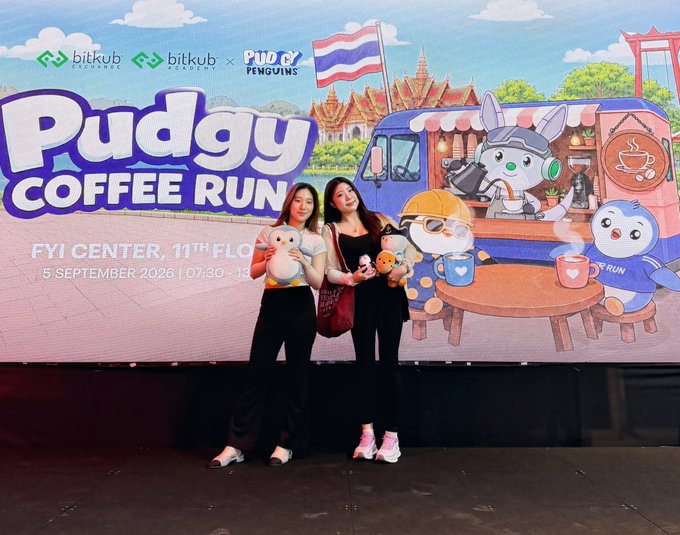Two women posing in front of a large promotional backdrop for the 'Pudgy Coffee Run' event at 'FYI CENTER, 11TH FLOOR' on '5 SEPTEMBER 2026', sponsored by Bitkub and Pudgy Penguins.