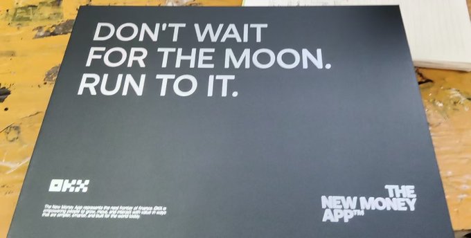 A dark promotional poster displays the motivational text "DON'T WAIT FOR THE MOON. RUN TO IT." along with logos for "OKX" and "THE NEW MONEY App" in the bottom corners.