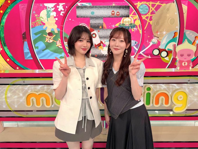 Two young Japanese women pose with peace gestures and cheerful expressions on a vibrant pink TV studio set, with "m" and "ing" letters visible behind them, promoting Manafi to's "#Monitoring" program airing at 7 PM.