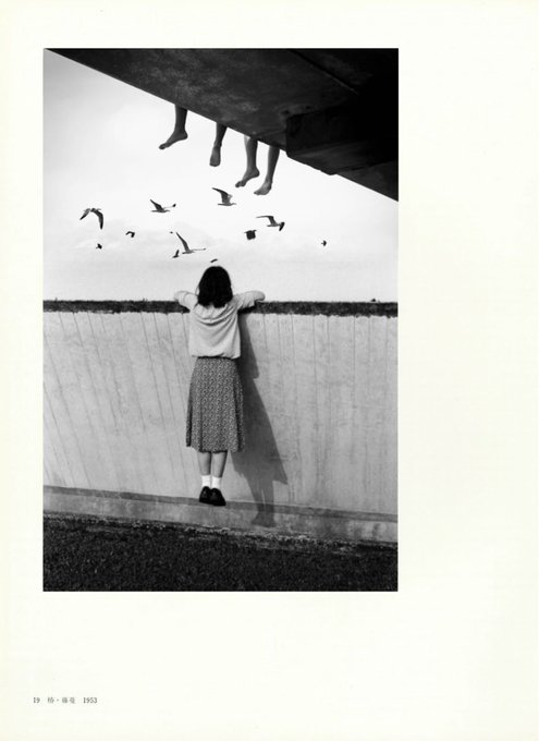 A surreal black-and-white photograph showing a young woman in a skirt leaning against a wall, looking up at floating legs and birds in the sky; small text at the bottom left reads '19 10 陽春 1993'.
