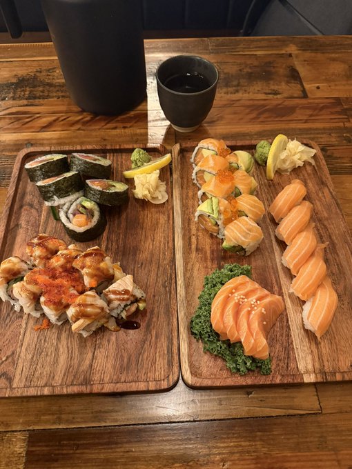 The image shows a wooden dining table with two trays of sushi arranged on top. One tray has six pieces of sushi while the other tray has four pieces. A cup of coffee is also present on the table, adding to the meal experience. The background appears to be a restaurant or cafe setting, suggesting that this could be a place where people can enjoy their meals and beverages in a relaxed atmosphere.