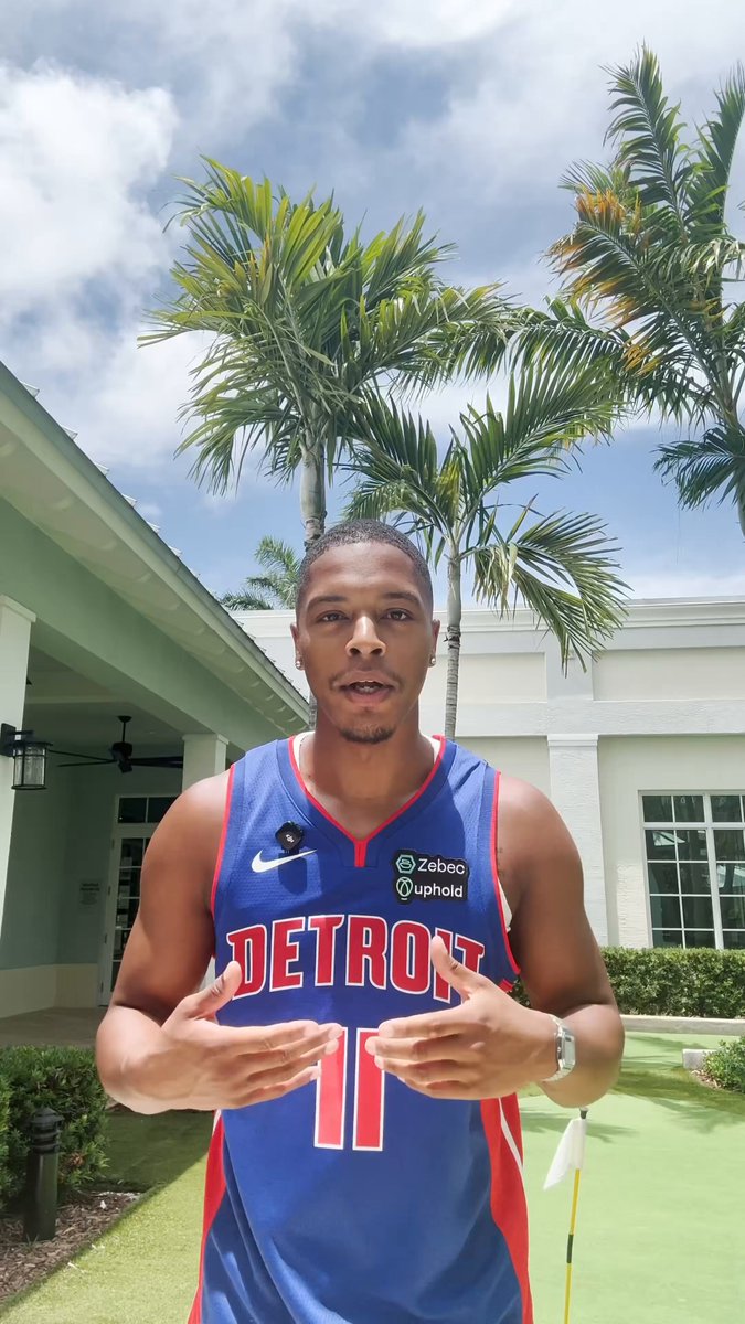 The image features a man wearing a blue Detroit Tigers jersey, standing outside with his hands at his sides. He appears to be posing for a photo or giving a speech. The background includes palm trees and a building, suggesting that he might be in an outdoor setting like a park or a golf course. There is also text on the image that reads "$ZBCN under a minute Reminder on tokenomics below". This could possibly be a promotional post for a basketball team or event related to the Detroit Tigers.

The man's attire and surroundings indicate that he might be involved in some form of sports-related activity, such as playing golf or attending a game. The presence of palm trees suggests that it is likely taking place in an area with a warm climate, like Florida or California.
