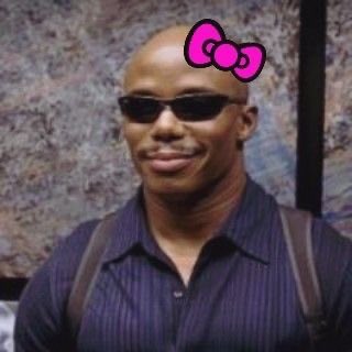 A man wearing sunglasses and a striped shirt with suspenders has a cartoon pink Hello Kitty bow edited onto his bald head, giving the image a humorous, meme-like edit. The post makes a crude joke comparing crypto traders' dexterity from long mouse use to a sexual act, using the bald man's image to jokingly represent the stereotypical "crypto bro."