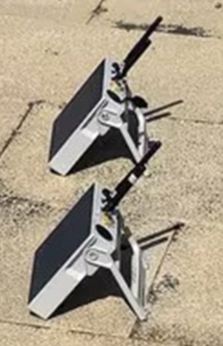 Two gray metal laptop stands with adjustable frames sit collapsed on a concrete surface, designed for portable use with folding legs.