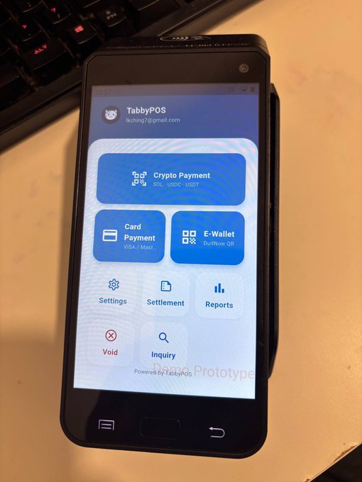 A handheld point-of-sale device branded "TabbyPOS" displaying a menu with payment options including "Crypto Payment" (SOL, USDC, USDT), "Card Payment", and "E-Wallet (DuitNow QR)".