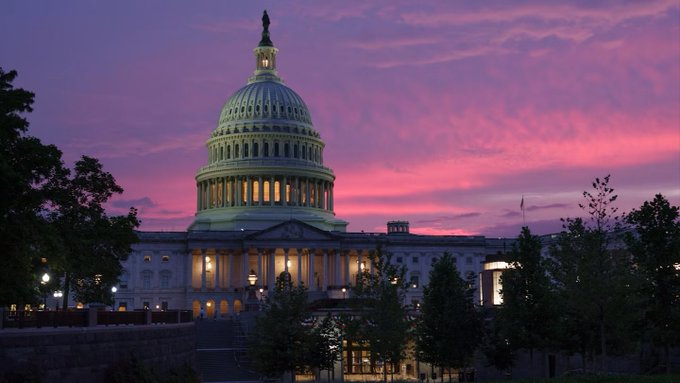 The United States Capitol building is illuminated against a vivid pink and purple sunset sky.