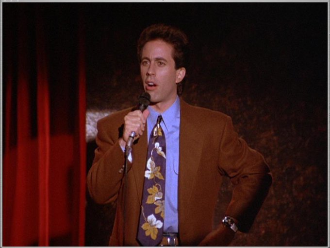 A stand-up comedian in a brown blazer and floral tie holds a microphone mid-joke on a dimly lit stage. The image humorously illustrates the post's mock "joke" about pumpfun being neither pump nor fun, framing the crypto platform's name as a punchline.
